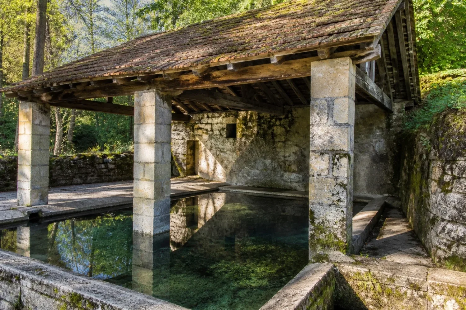 Lavoir en pierre couvert d'un toit de tuiles, avec un bassin d'eau claire, dans un village de Bourgogne.