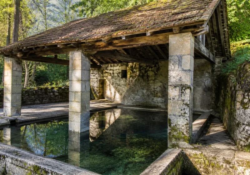 Lavoir en pierre couvert d'un toit de tuiles, avec un bassin d'eau claire, dans un village de Bourgogne.
