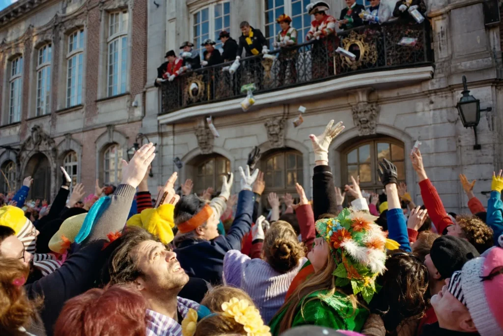 Foule costumée tendant les mains sous le balcon de l'hôtel de ville pendant le jet de harengs.