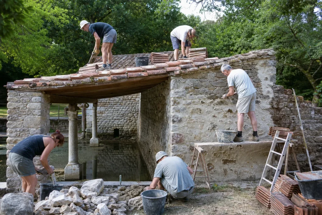 Bénévoles d'une association restaurant un lavoir en pierre, rejointoiement à la chaux et tuiles.